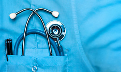 A close-up photo of the pocket on a doctor's scrub shirt, containing a folded-up stethoscope and a pen-light.